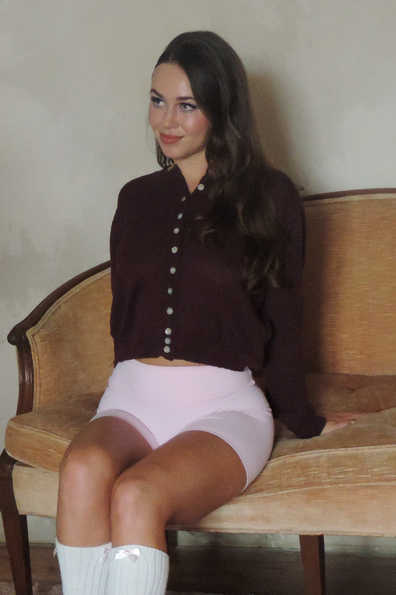 Woman sitting on a wooden bench with a pink balloon in a room in a Frequency Skin outfit.